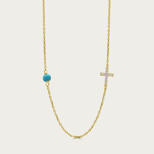 A gold-colored necklace featuring a small cross charm and a blue bead on a chain.